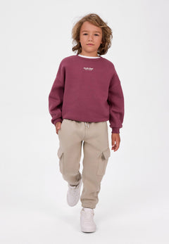Child wearing cream cargo joggers with flap thigh pockets and a berry sweatshirt.