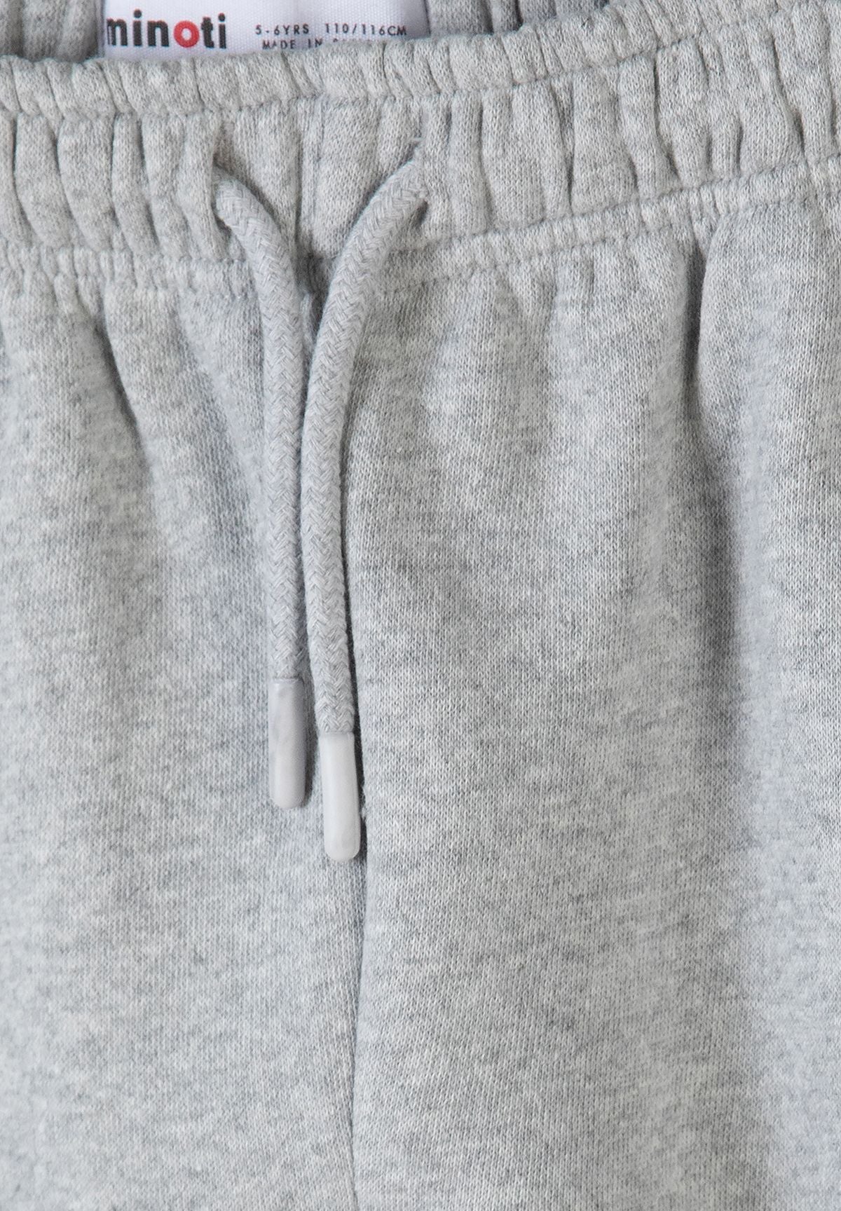 Lichtgrijze trainingsset voor jongens met een hoodie met rits en een joggingbroek, detail van de tailleband met trekkoord.