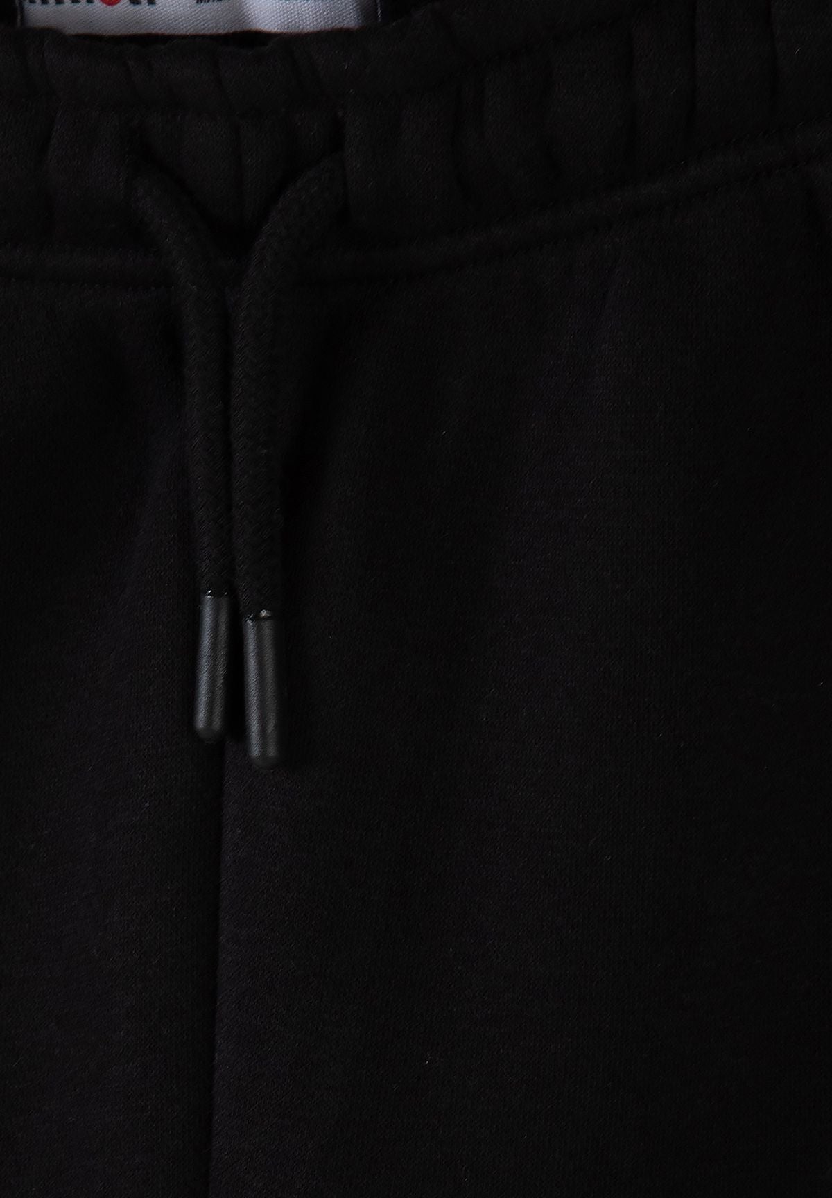 Zwart trainingspak voor jongens met een hoodie met rits en een joggingbroek, detail van de tailleband met trekkoord.