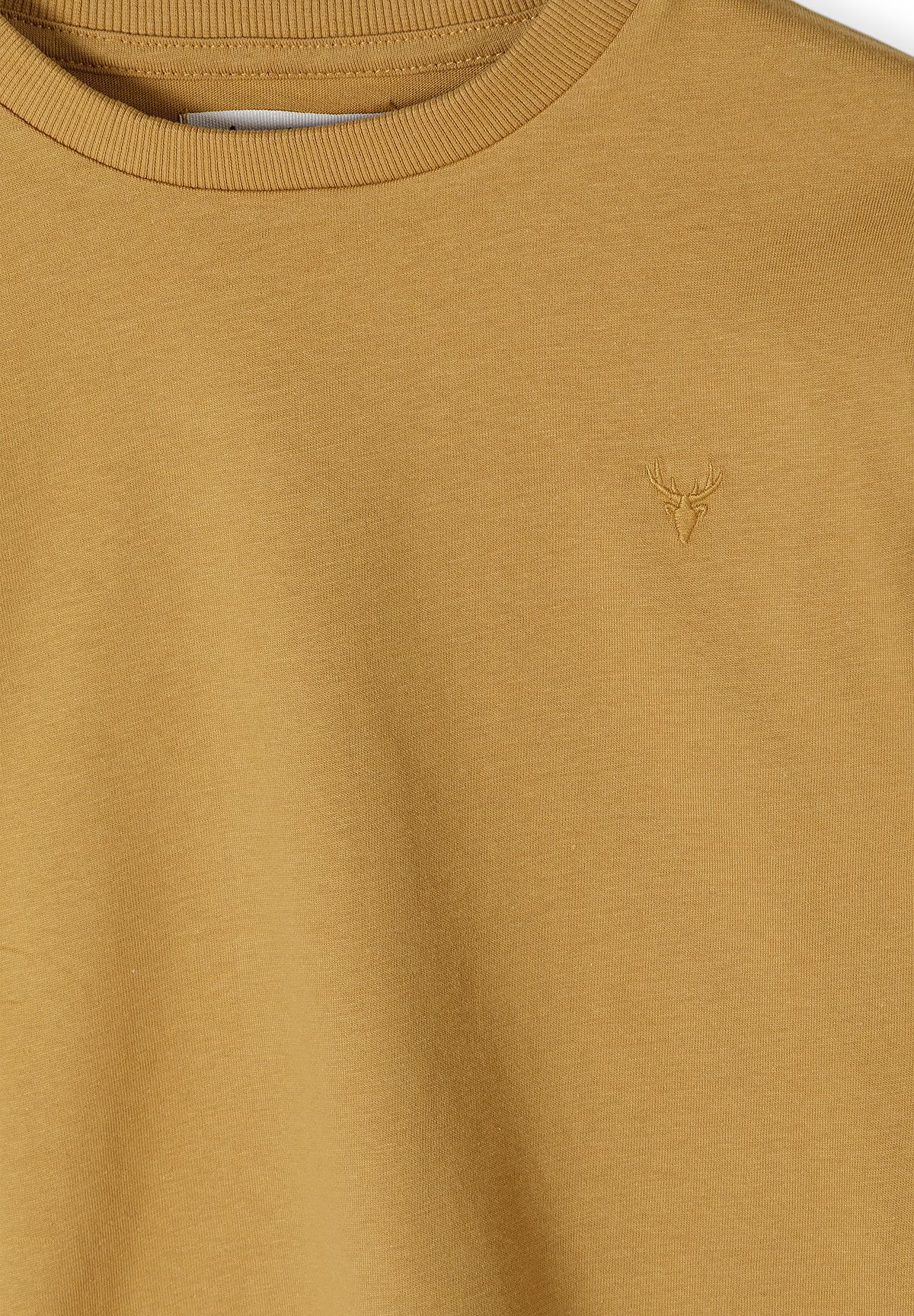 Close-up of tonal embroidered stag head on mustard long-sleeved top near the crew neck.