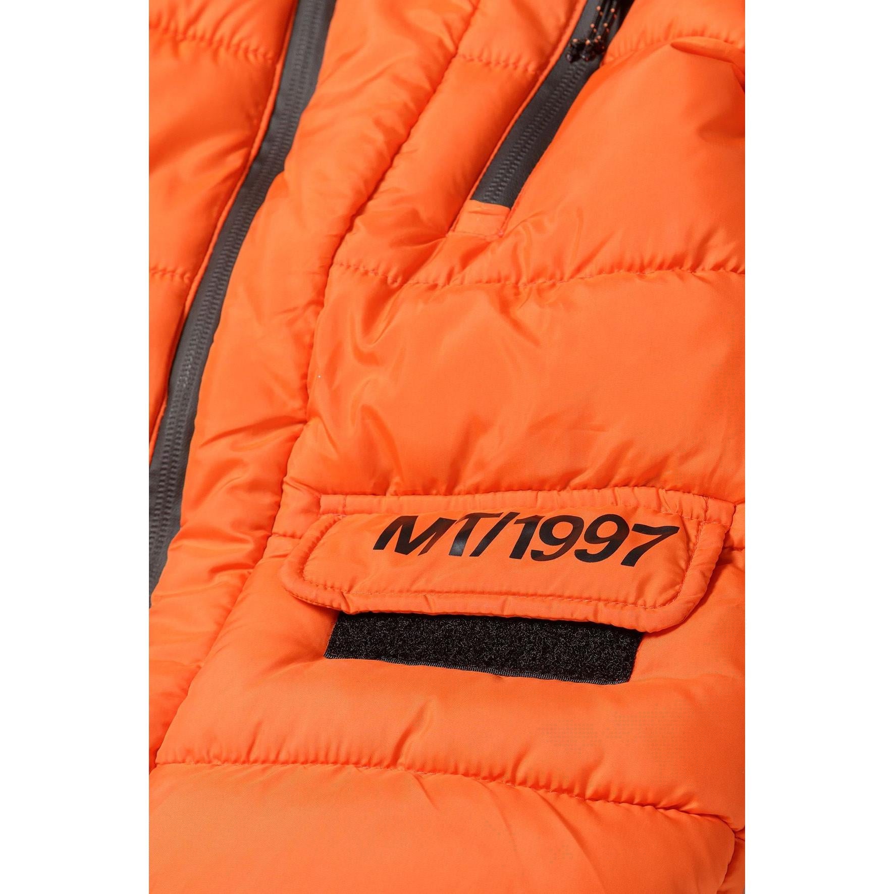 Close-up detail of orange padded jacket showing MT1997 branding patch, quilted texture, zip closures and black trim details