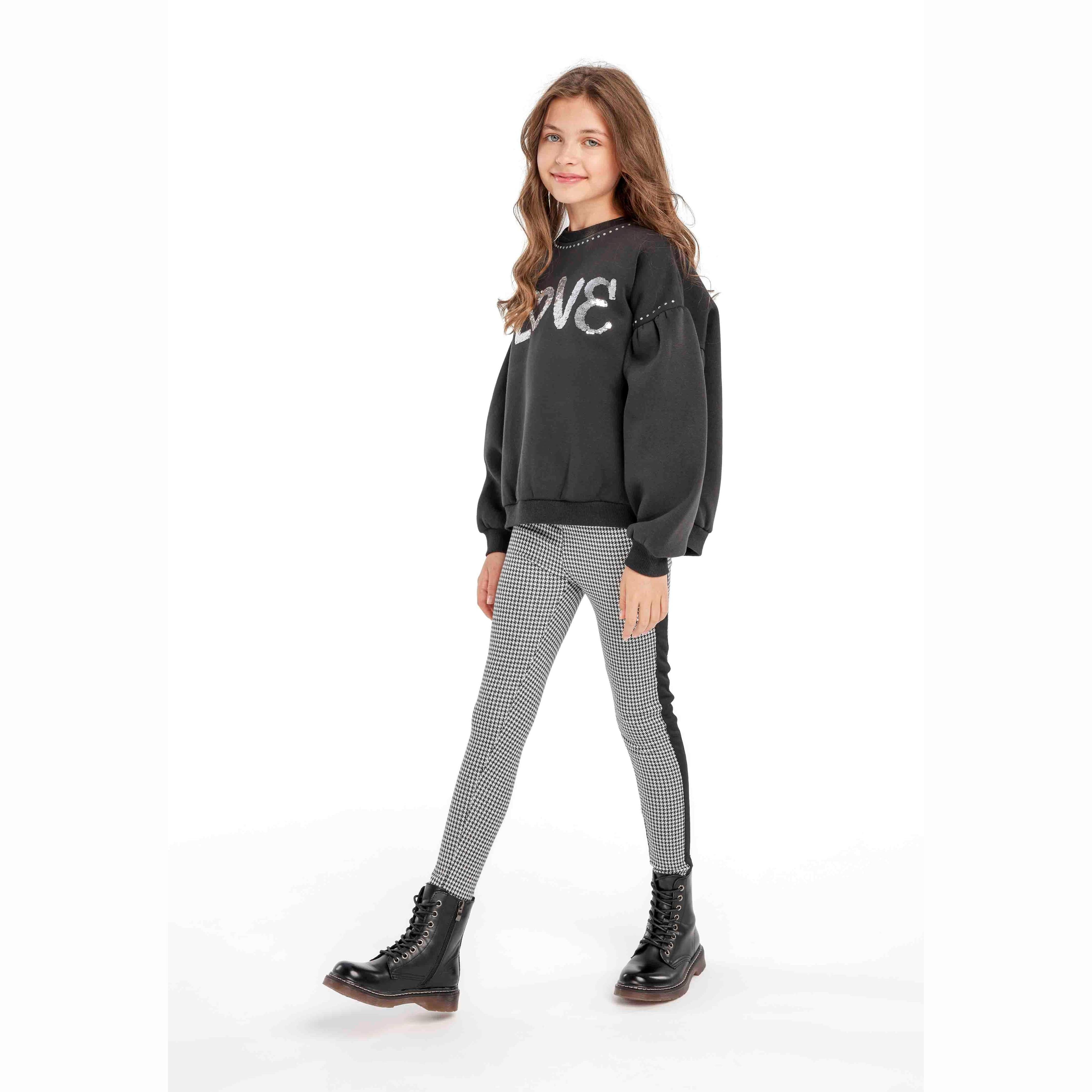 Girl wearing black LOVE sweatshirt and black white dogtooth leggings with black combat boots on white background