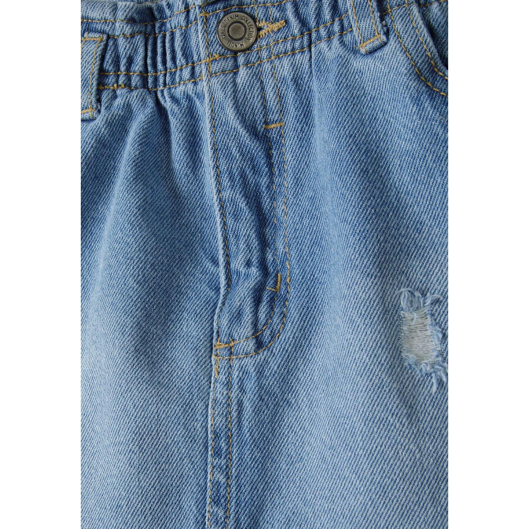 Close-up detail of denim skirt showing paperbag waistband construction, button closure with Minoti branding and distressed fabric texture