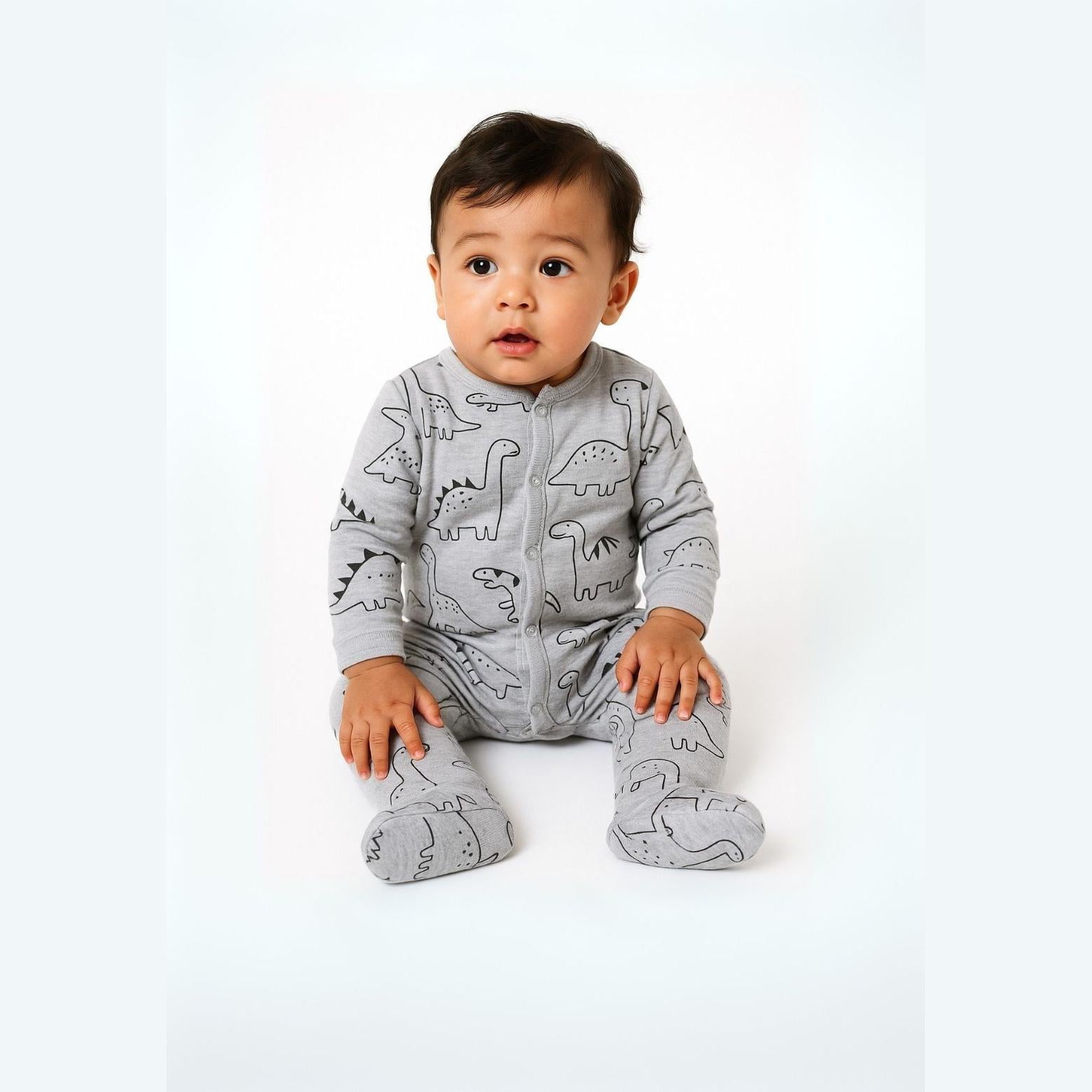 Baby wearing grey sleepsuit with black dinosaur print sitting on white background