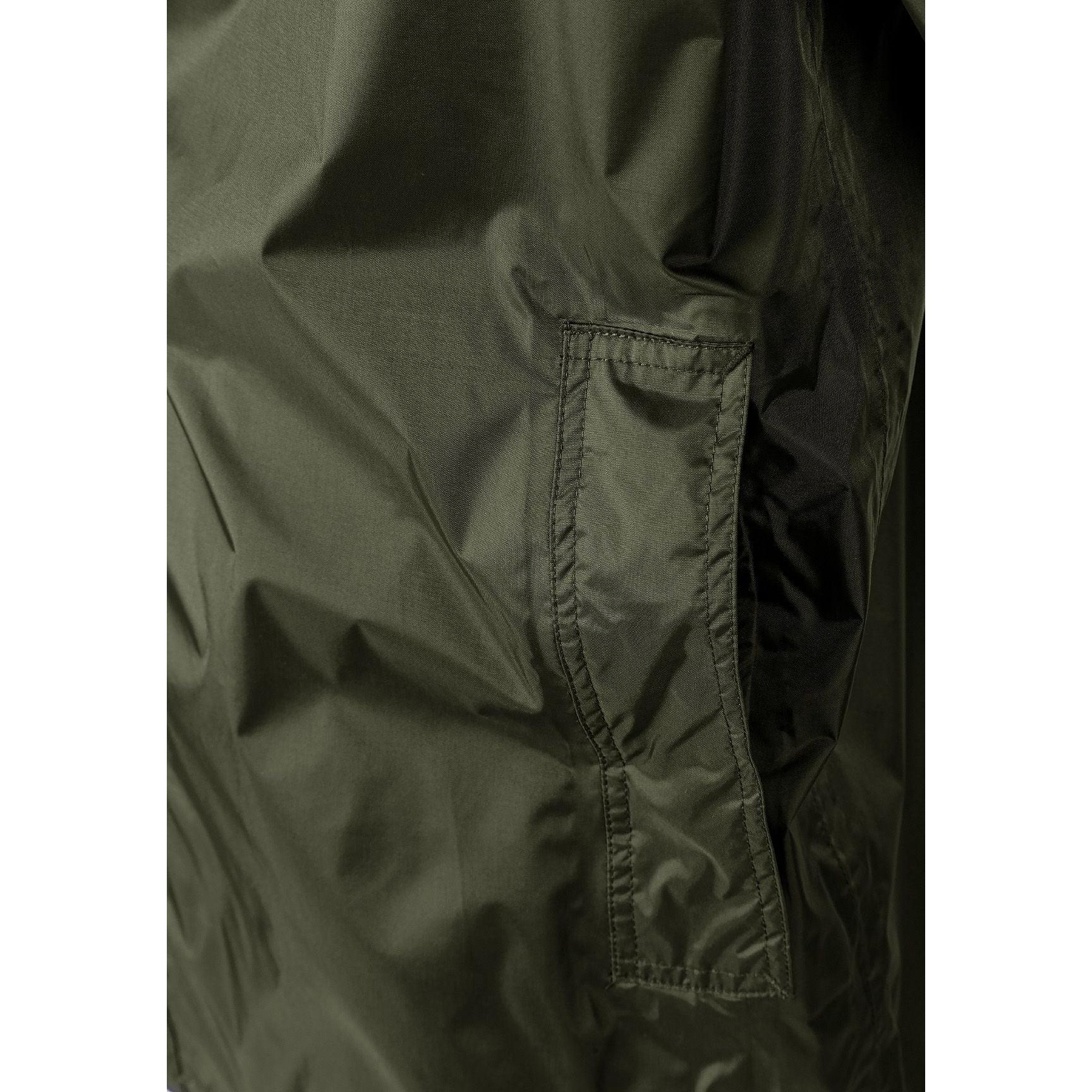 Close-up detail of khaki jacket side showing zip pocket with branded zipper pull and seam construction against white background