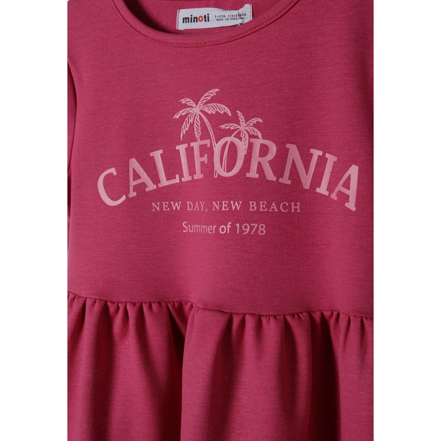 Close-up detail of pink dress showing California beach print with palm trees and text, plus Minoti brand label at neckline