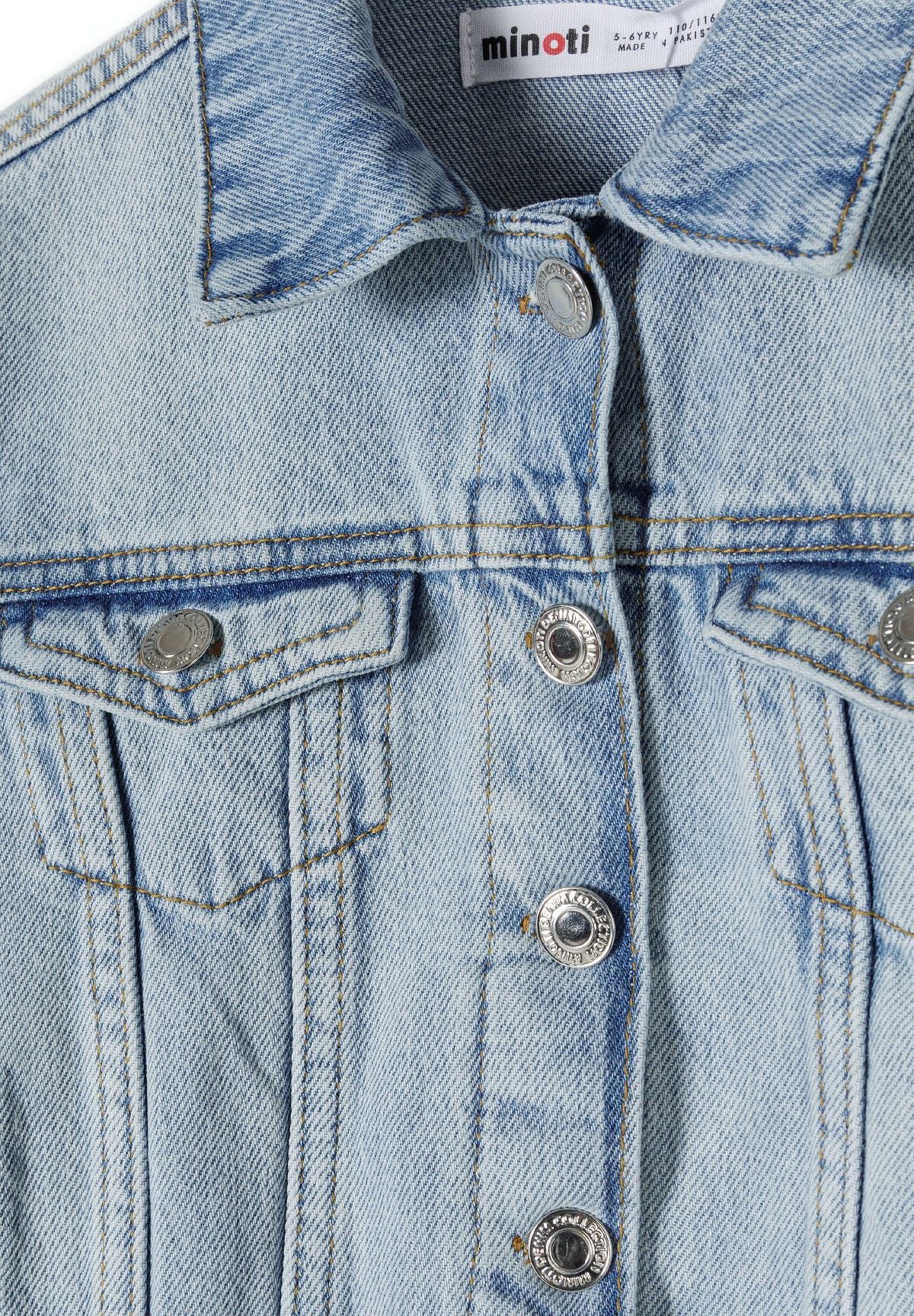 Close-up of the button and chest pocket on the light blue denim jacket.