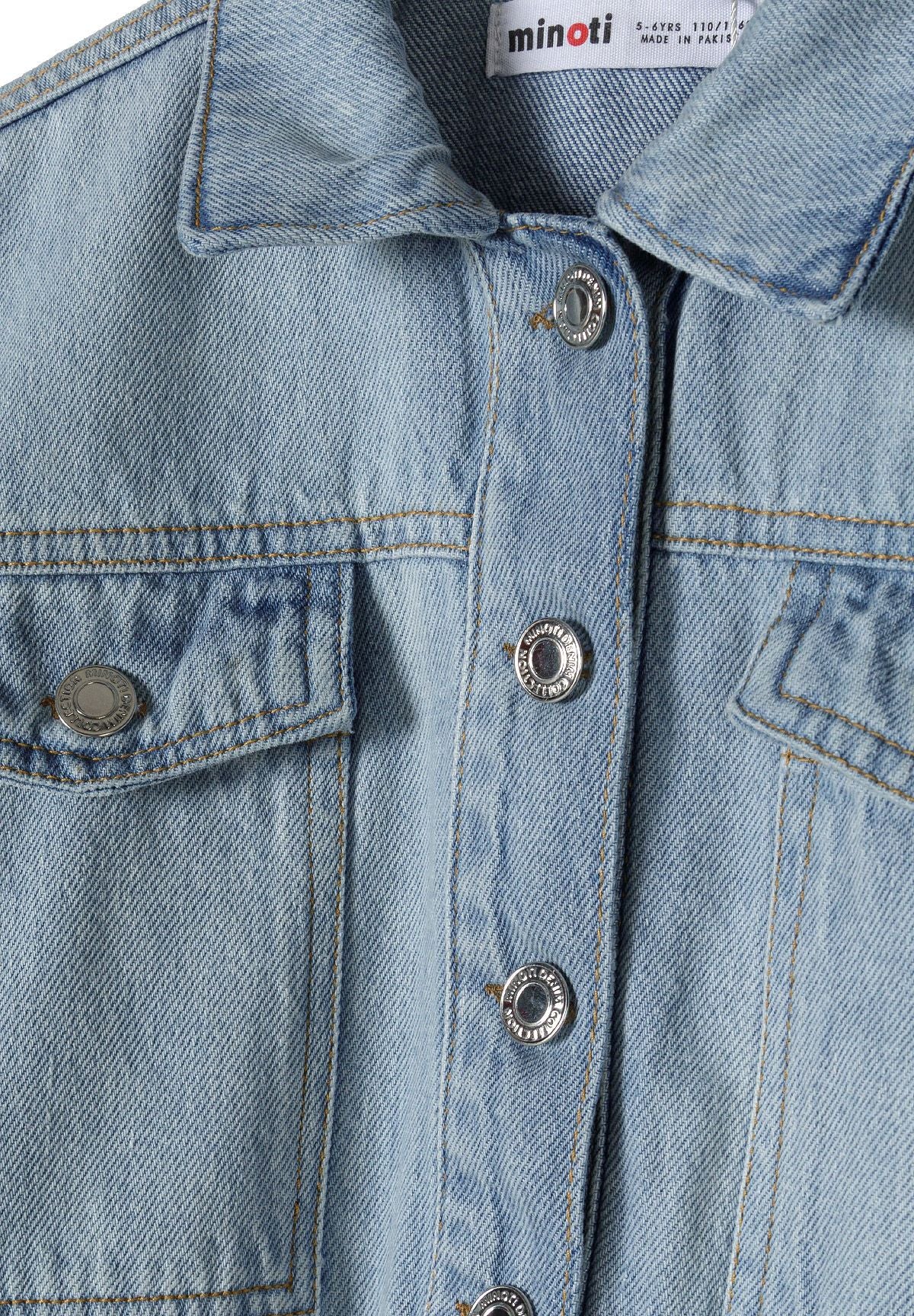 Close-up of the button and chest pocket on the light blue denim jacket.