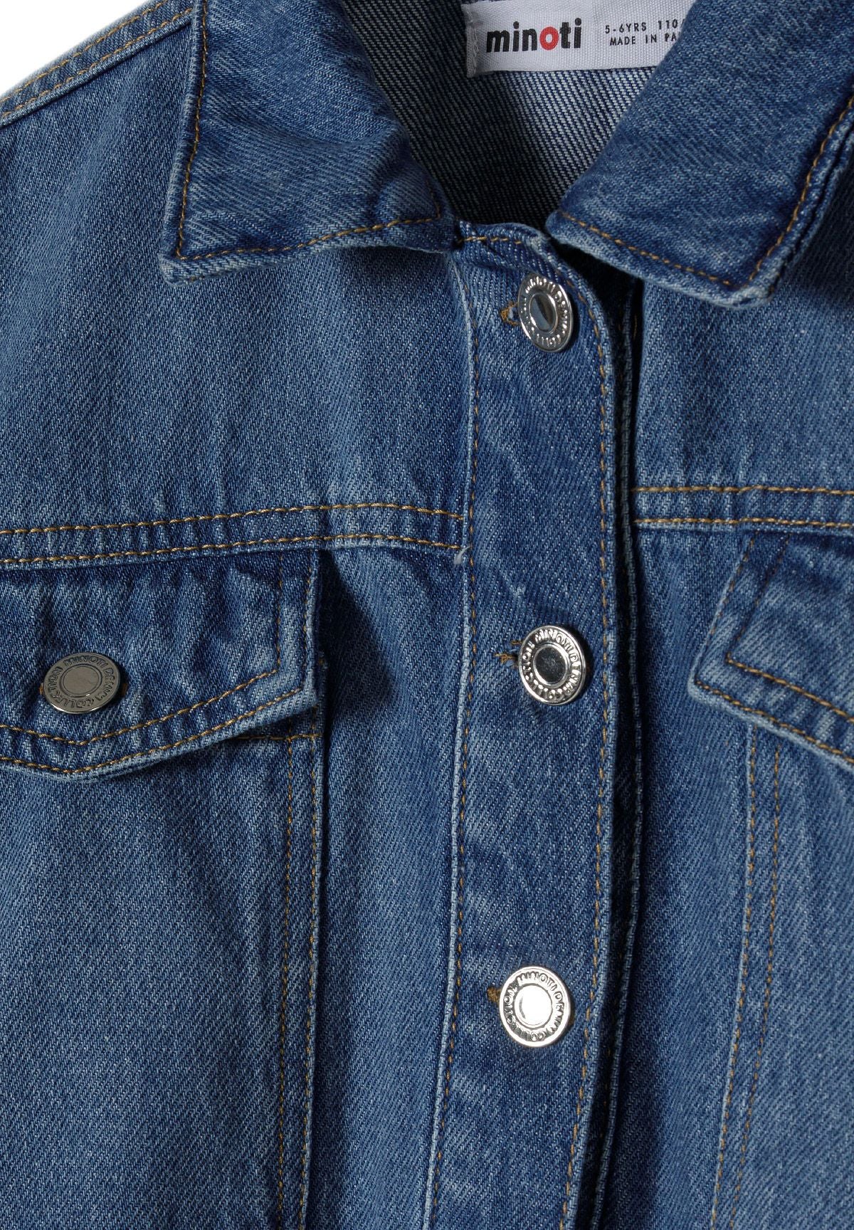 Close-up of the button and chest pocket on the blue denim jacket.