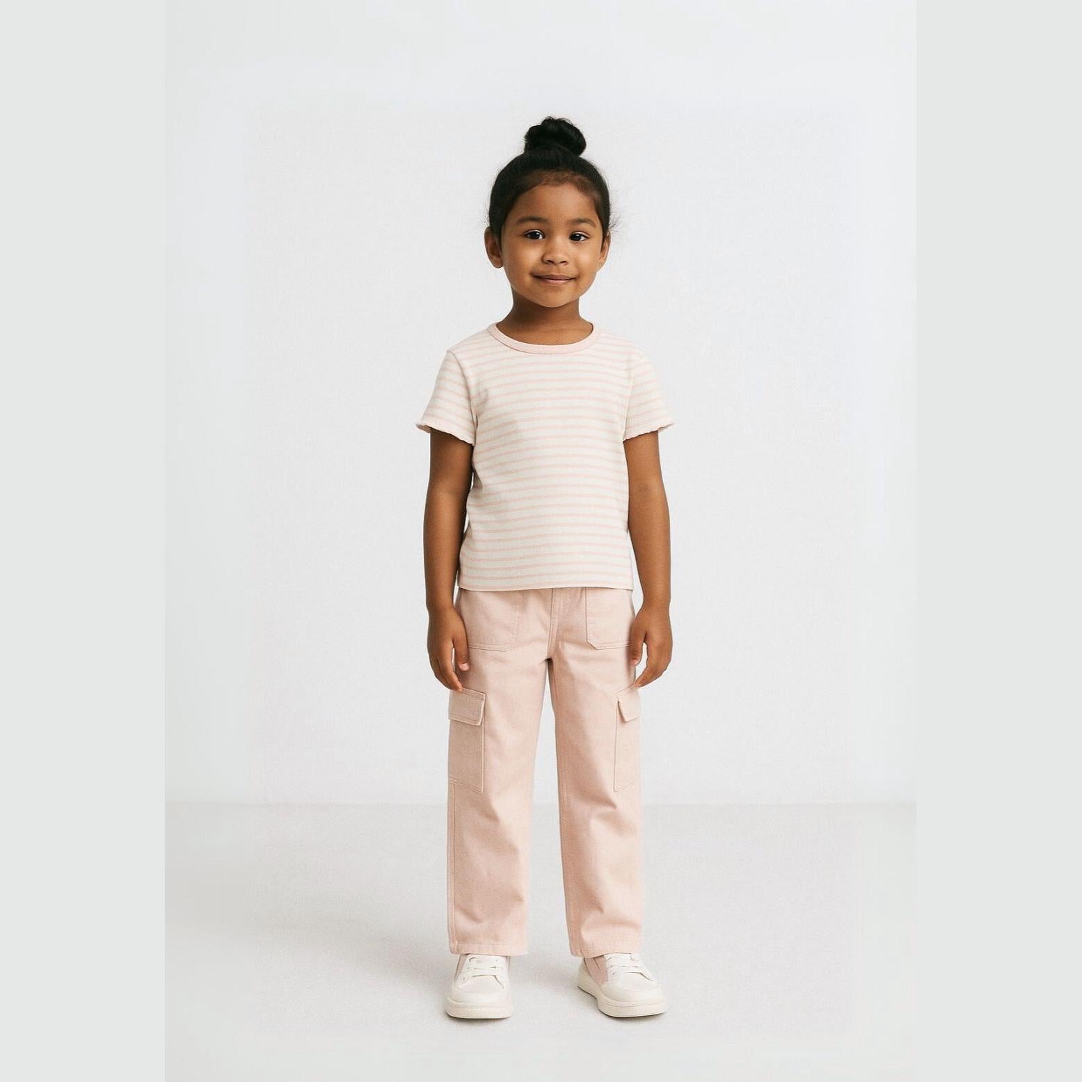 Young girl wearing pink striped t-shirt and wide leg cargo trousers in soft pink, standing against white background