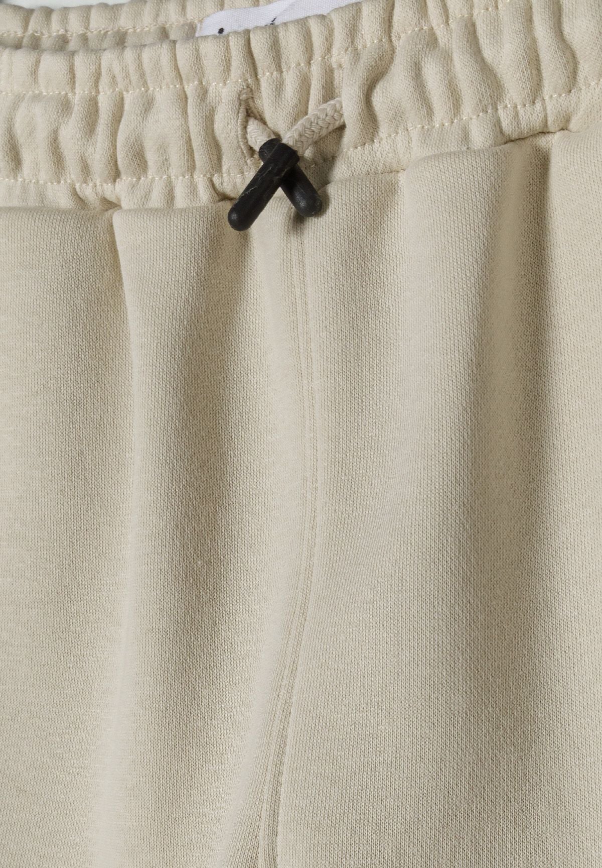 Detail of shorts with elasticated waistband and drawstrings in neutral color.