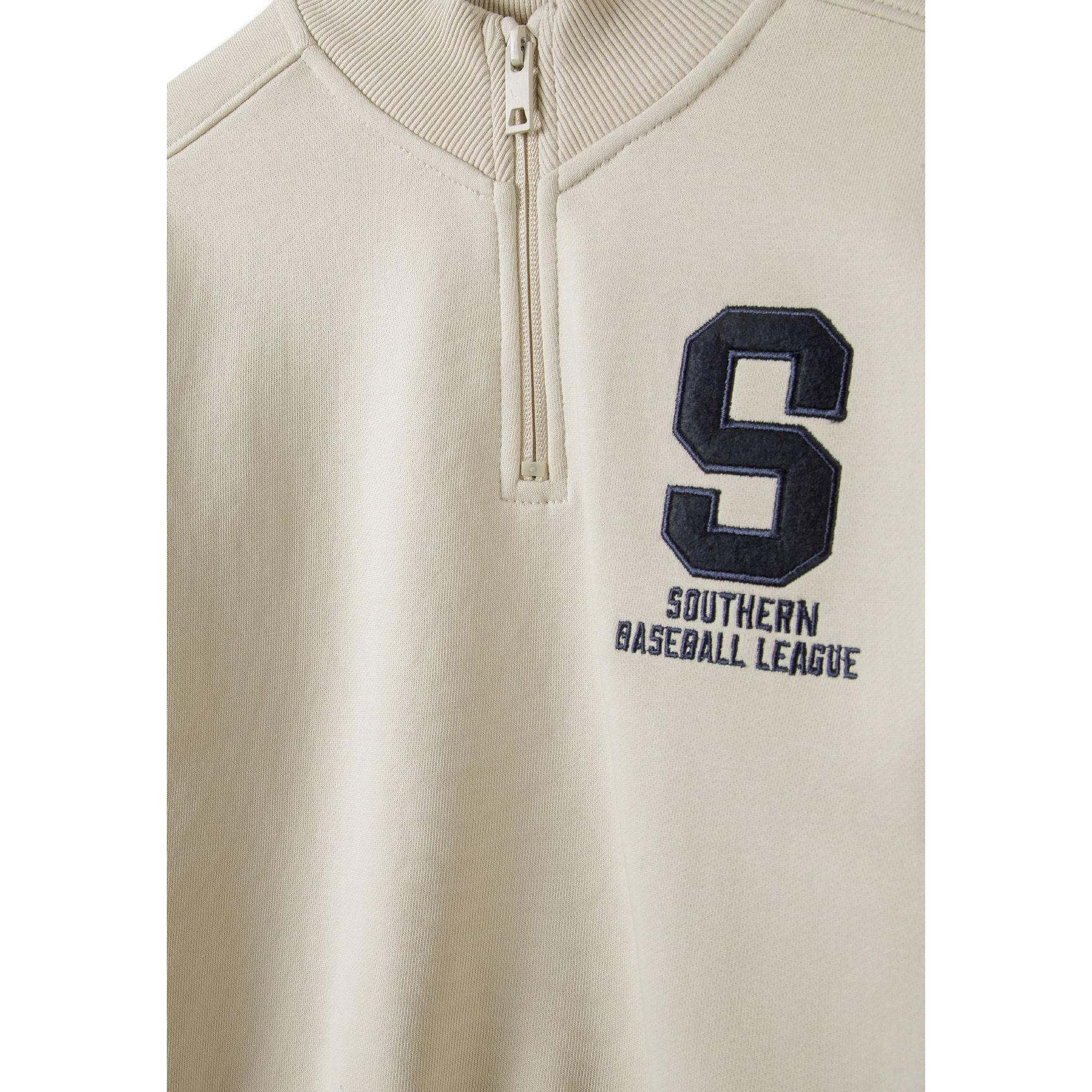 Close-up detail of cream sweatshirt front showing half-zip closure and large letter S with Southern Baseball League text embroidered on chest