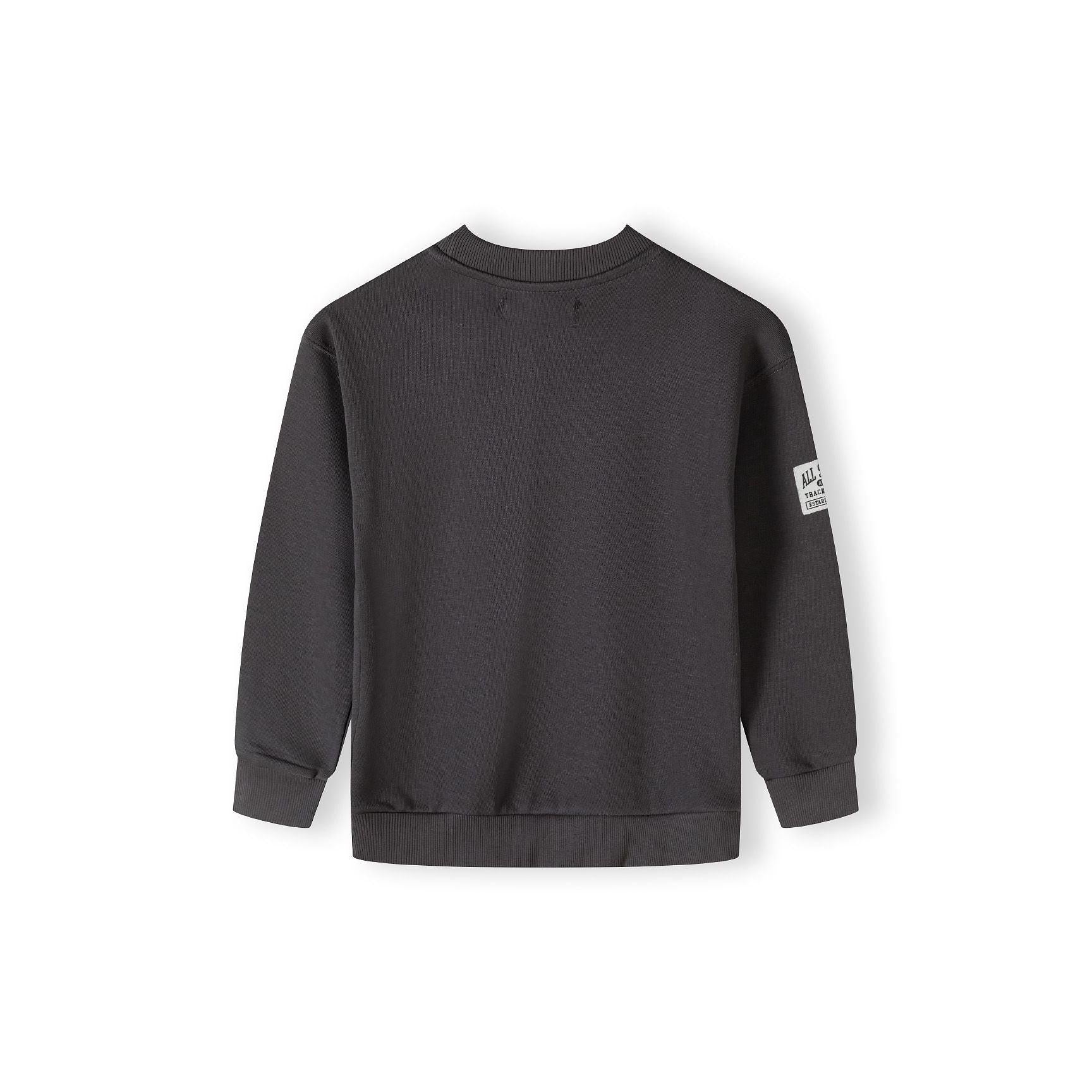 Back view of grey crew neck sweatshirt showing plain design with small white label patch on sleeve against white background