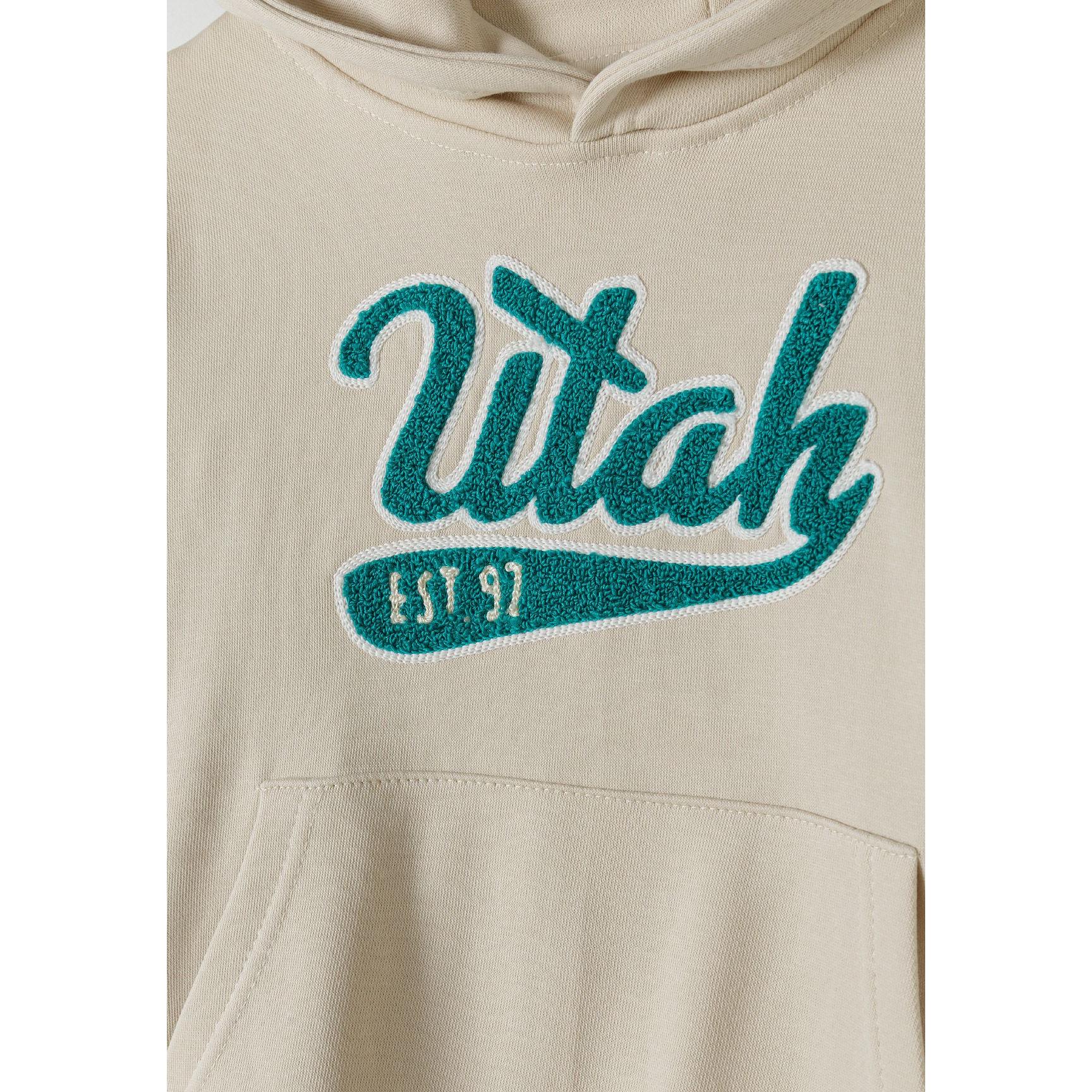 Close-up detail of Utah embroidered logo in teal on cream hoodie fabric