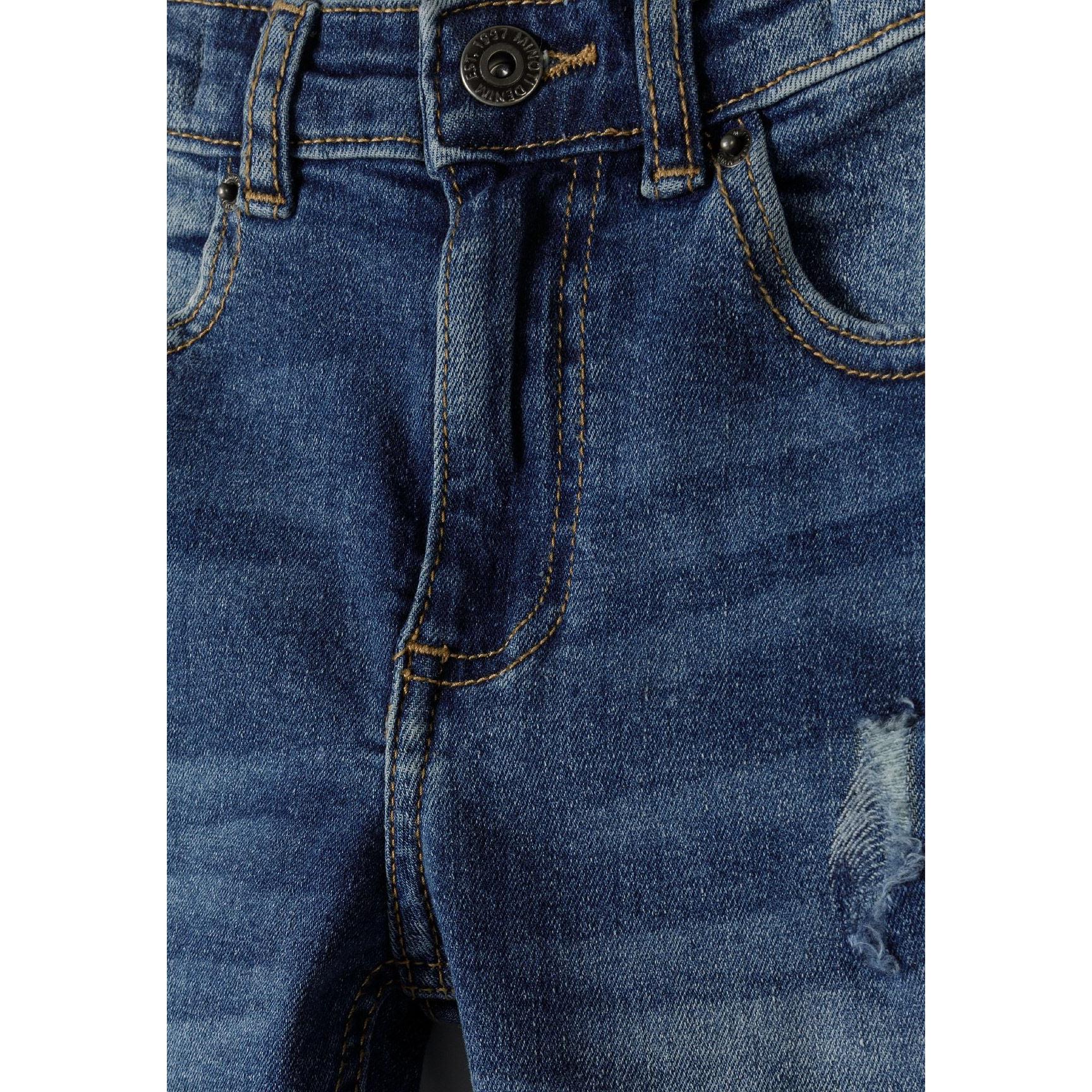 Close-up detail of navy jeans waistband and front pocket area showing ripped distressing and button closure