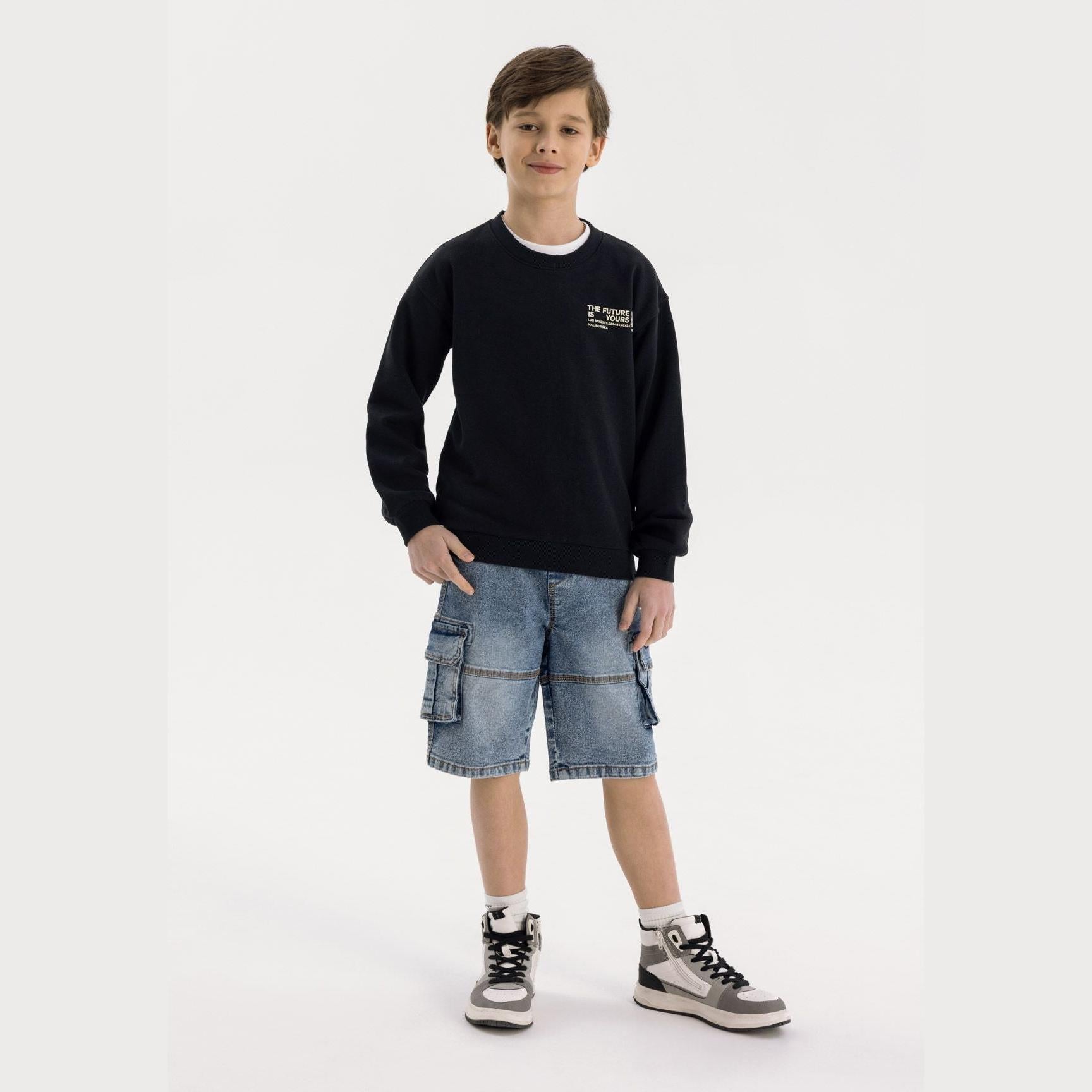 Young boy wearing navy denim cargo shorts with black sweatshirt, standing on white background