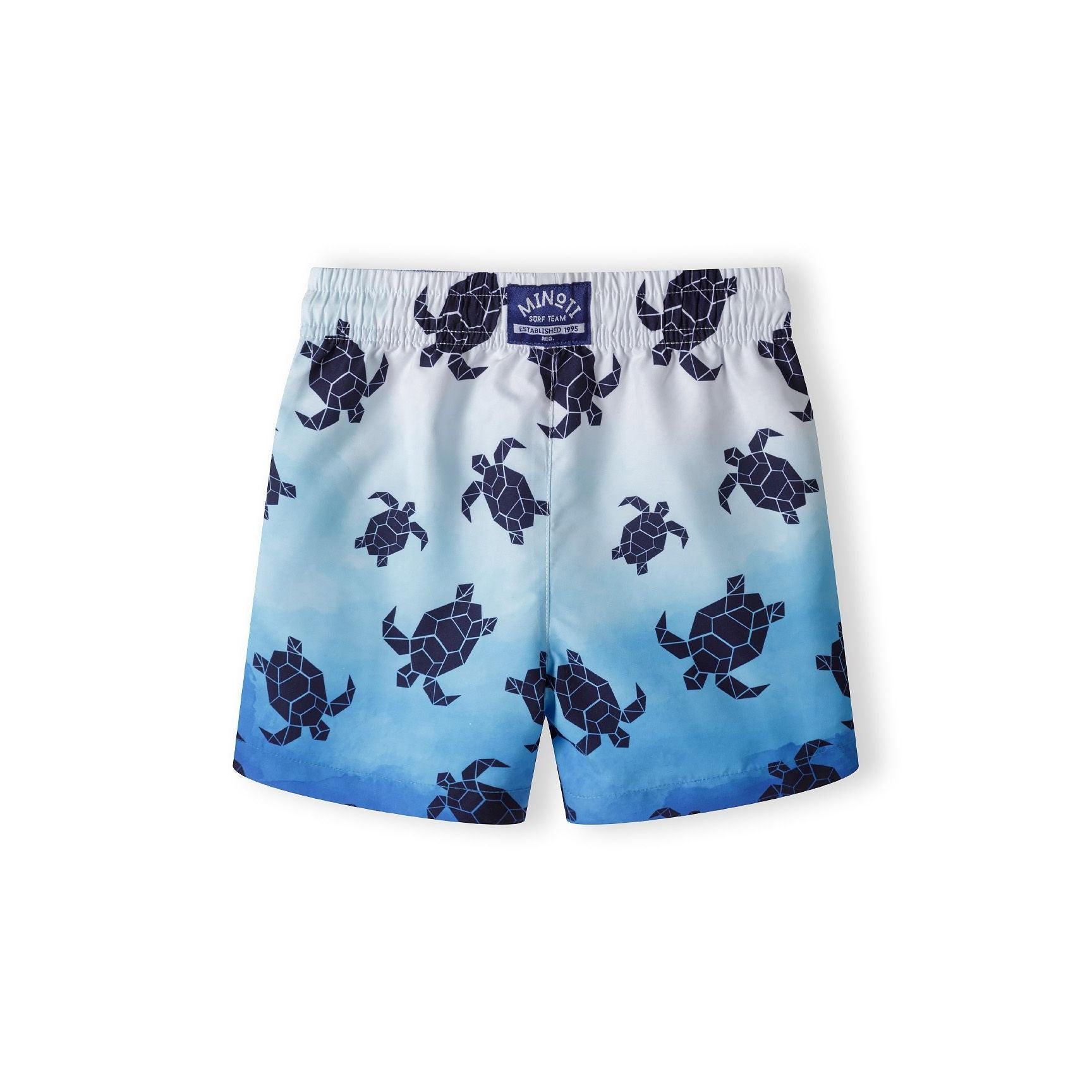 Back view of swim shorts displaying gradient blue fade effect and scattered turtle motifs with Minoti brand label visible