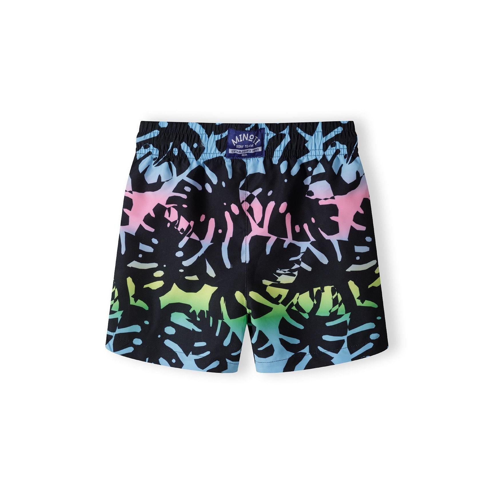 Back view of the same black board shorts showing Minoti brand label on waistband and continuation of colorful tropical leaf pattern on white background