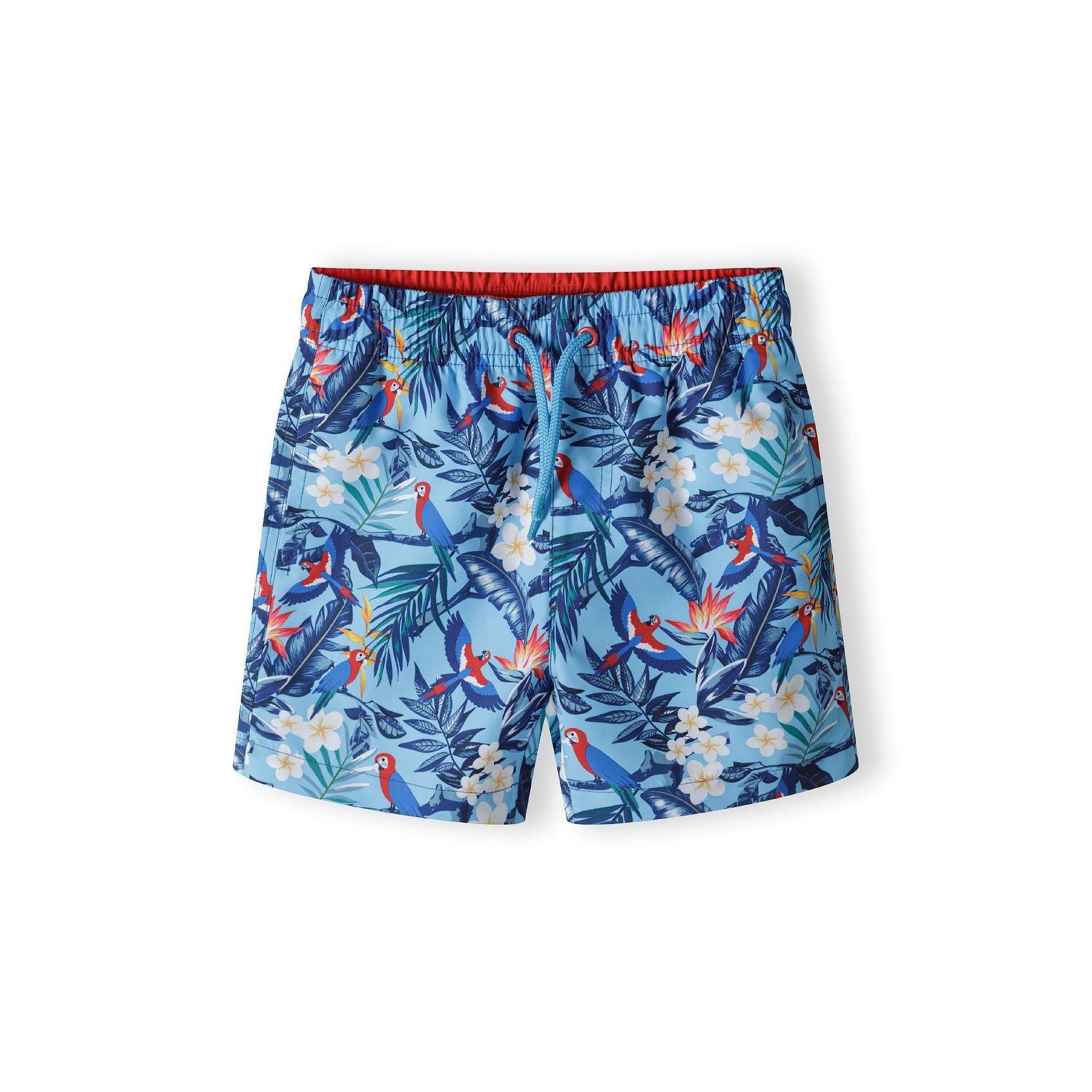Blue swim shorts with tropical print featuring colourful parrots and palm leaves, flat lay view against white background
