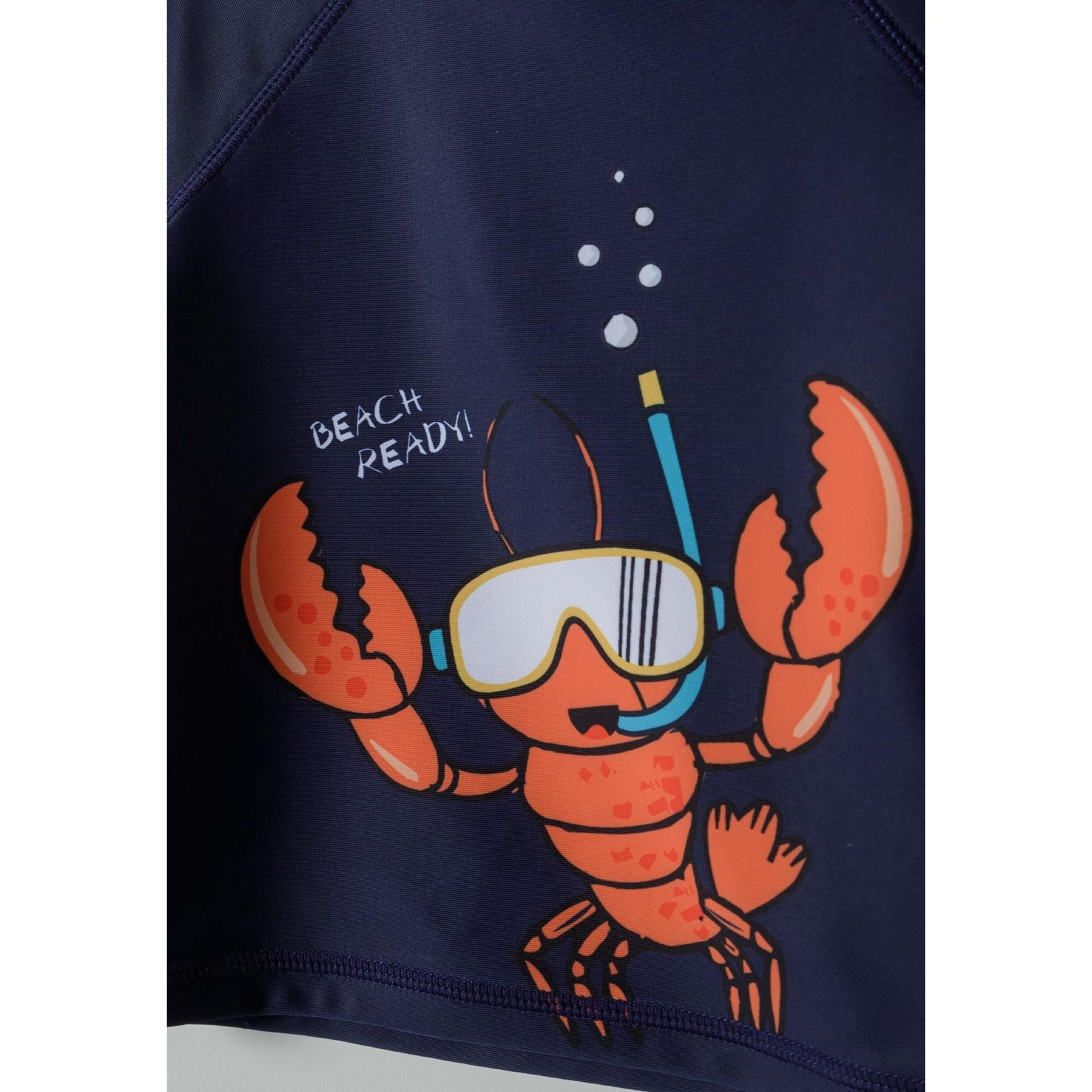 Detail view of navy rashguard top showing orange snorkelling lobster character with diving mask and 'Beach Ready' text with bubble effects