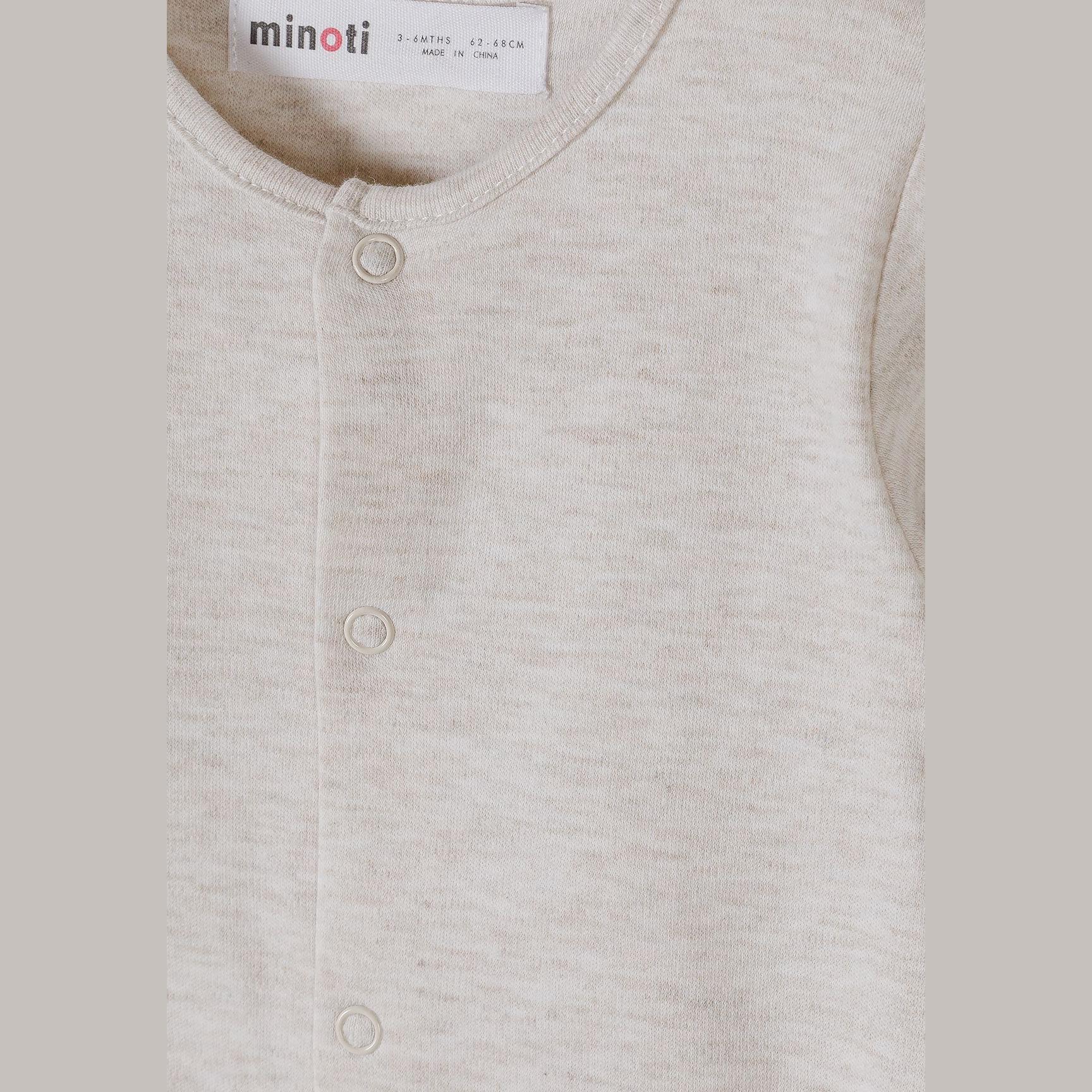 Close-up detail of cream sleepsuit showing Minoti label, snap button closure and soft cotton texture with ribbed neckline