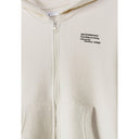 Close-up detail of cream hoodie showing zip closure, small text print on chest area, kangaroo pocket opening and soft cotton fabric texture