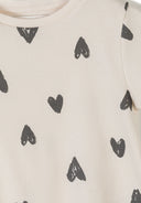 Close-up detail of cream ribbed fabric texture showing hand-drawn black hearts print pattern and crew neckline