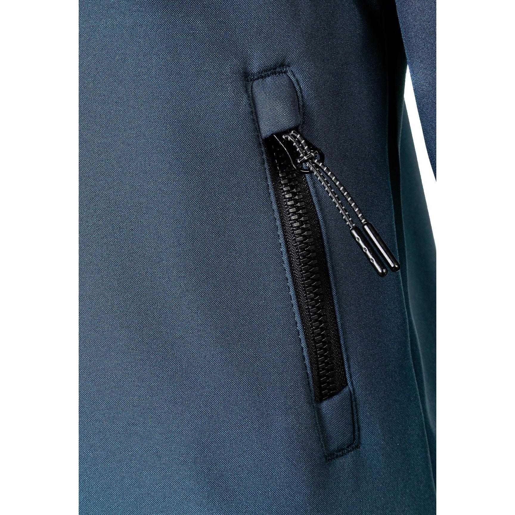 Close-up detail of teal softshell jacket showing black zippered side pocket with zipper pull