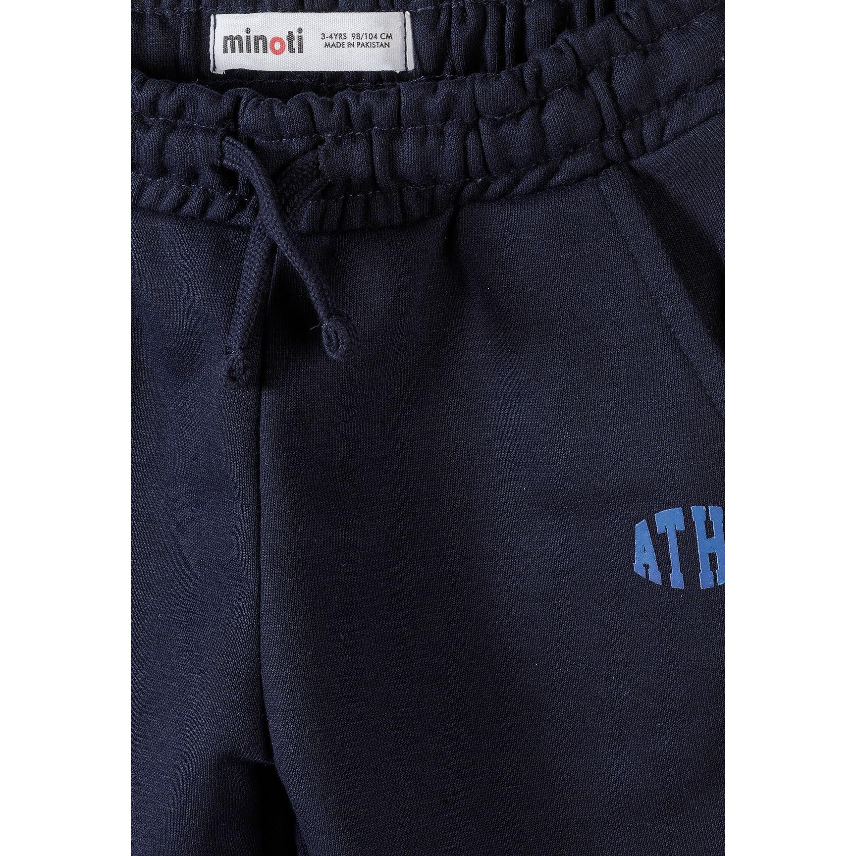Detail shot of navy joggers waistband showing Minoti label, elasticated waist construction with drawstring, and partial view of blue ATHL logo on leg