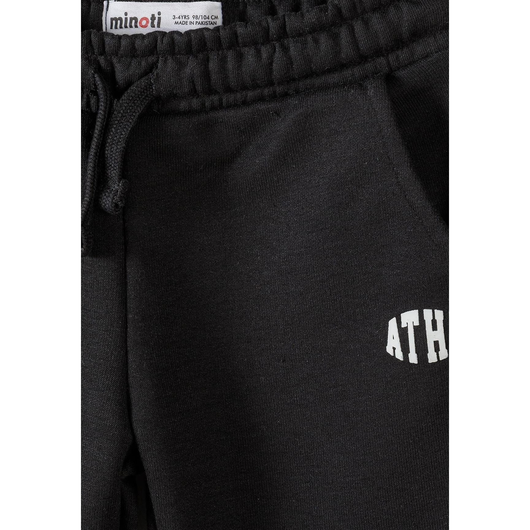 Close-up detail of black joggers showing Minoti label, drawstring elastic waistband and white ATHL lettering on the leg