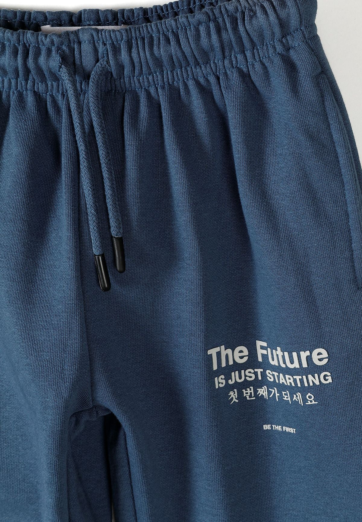 Detail of boys' blue tracksuit trousers with elasticated waistband and printed text.