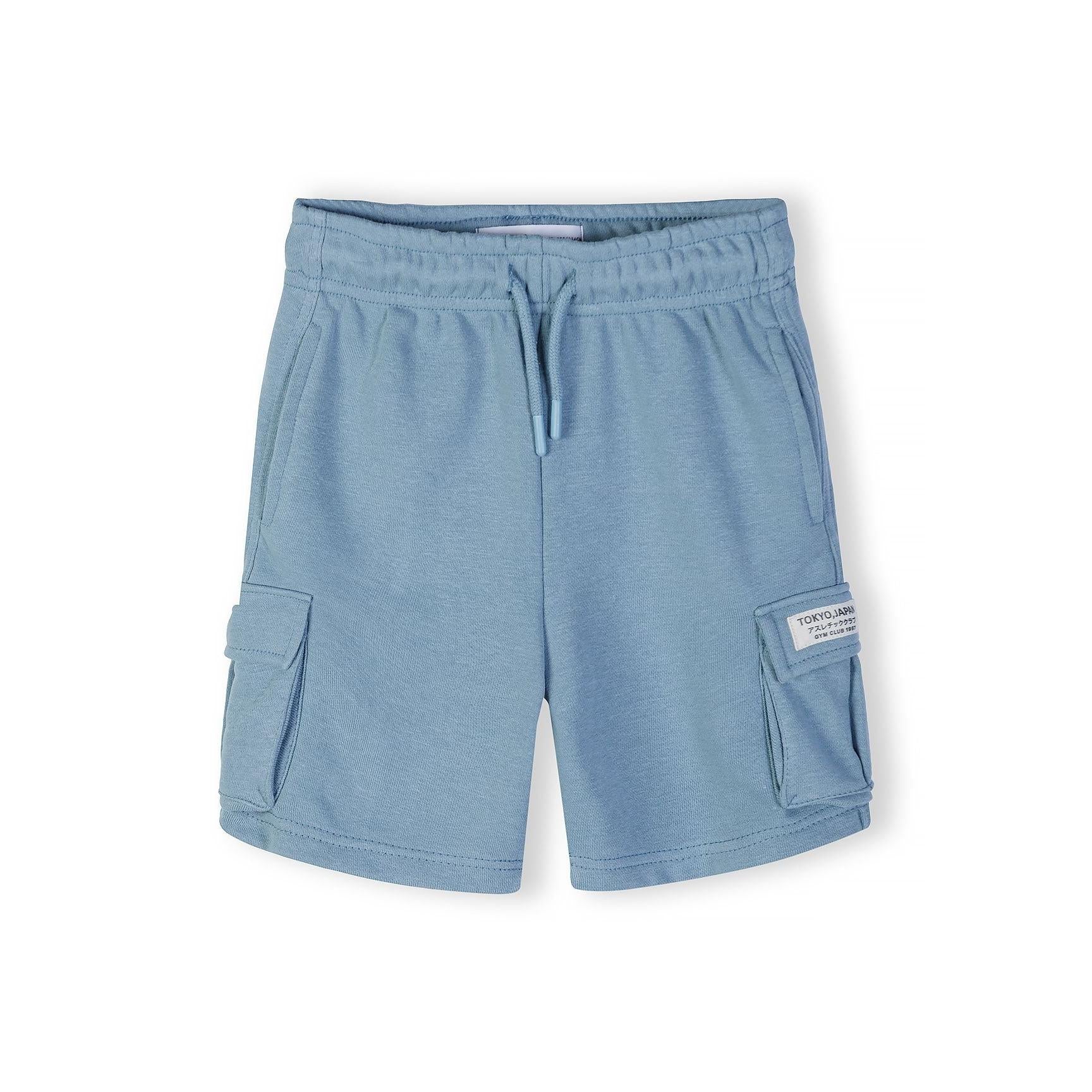 Close-up detail of front chest area showing circular 'The Future is Now' text print with Japanese characters on blue grey fabric