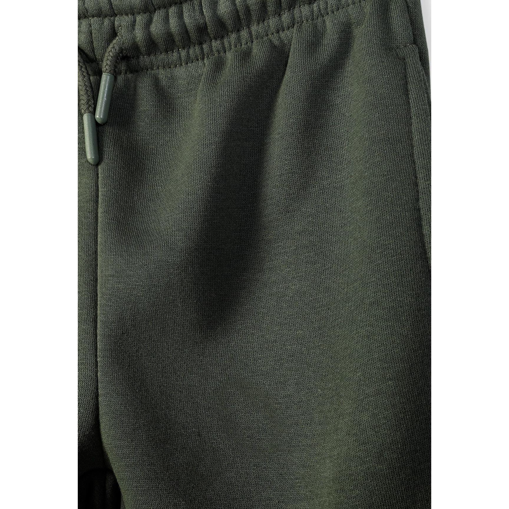 Close-up detail of khaki jogger waistband showing elasticated band with drawstring and fabric texture on white background