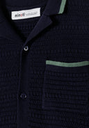 Detail of a boys' navy blue knitted polo shirt with a collar and chest pocket.