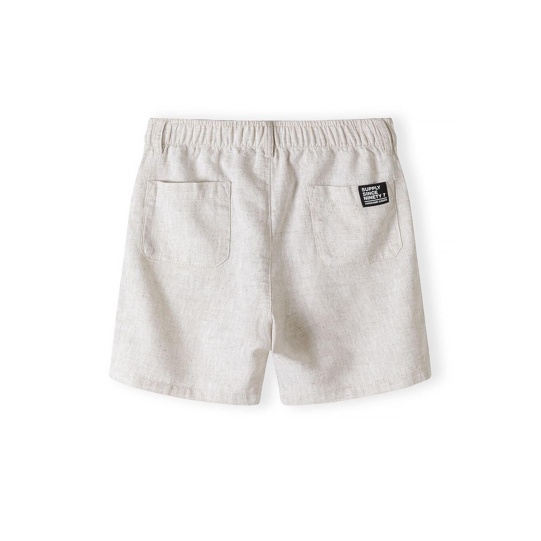 Close-up detail of light blue knitted polo shirt showing Minoti label, three wooden buttons on placket and white collar trim