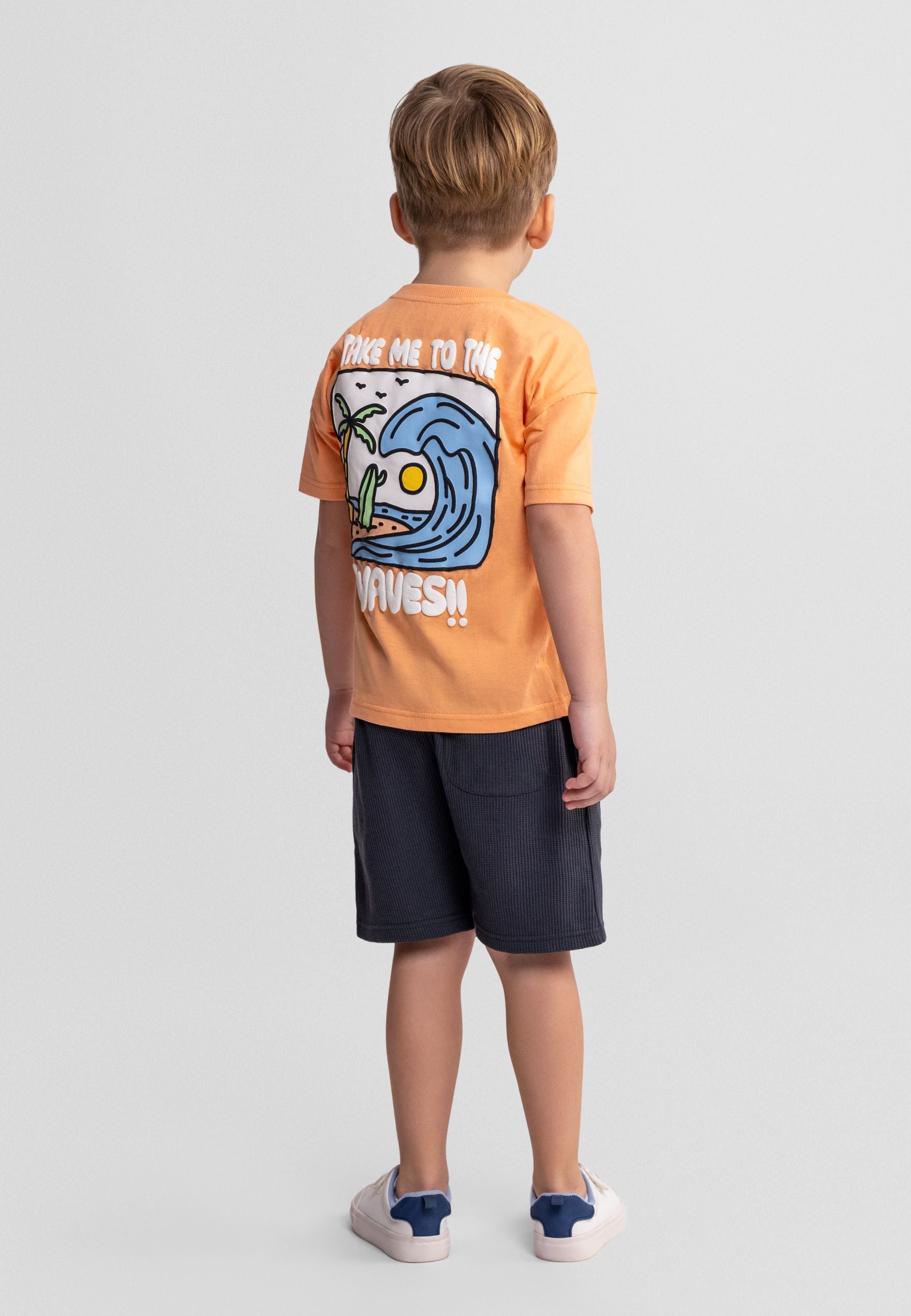 Apricot cotton t-shirt laid flat showing surf crew graphic with palm tree and wave design on chest area against white background