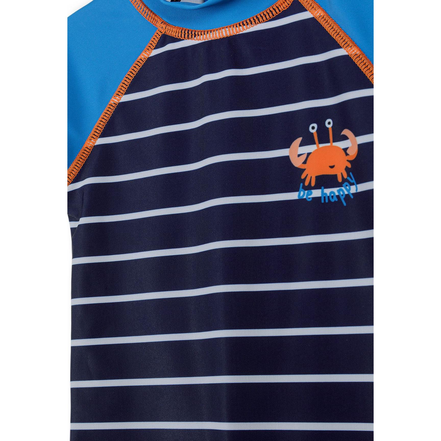 Close-up detail of swimsuit chest showing orange crab graphic with 'be happy' text on navy striped fabric with blue raglan sleeves