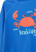 Blue kids rash vest with a playful orange crab design and "Beach Life" text for children’s fashion.