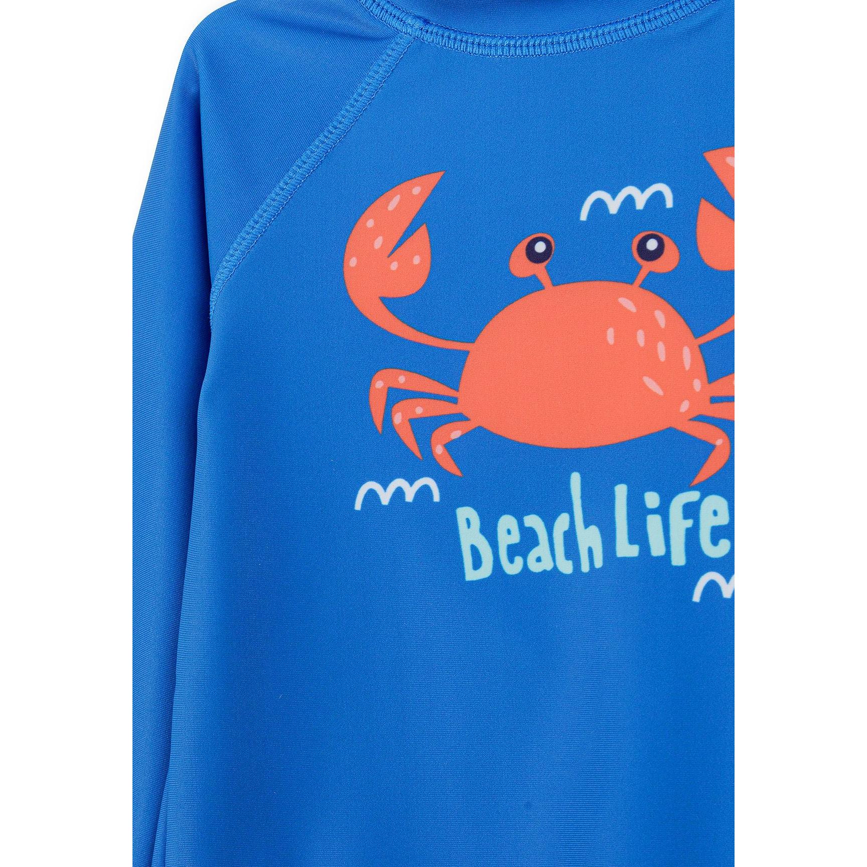 Detail view of blue rash vest showing orange crab graphic with Beach Life text and flatlock seams