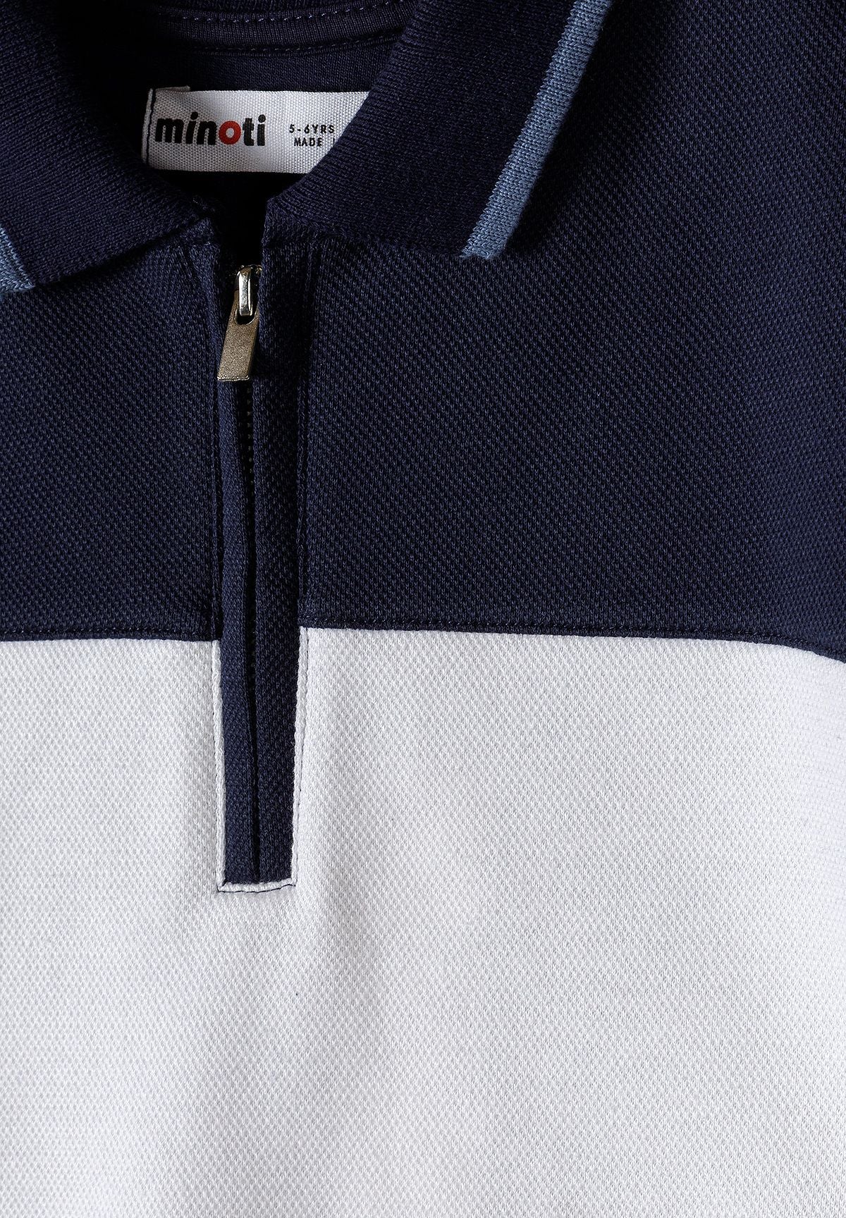 Close-up of a boys' navy and white polo with a zip collar and textured pique finish.