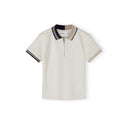 Close-up detail of cream pique polo shirt showing Minoti label, zip neck opening, navy collar and subtle embroidered logo on chest