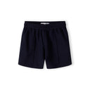 Close-up detail of cream pique polo shirt showing Minoti label, zip neck opening, navy collar and subtle embroidered logo on chest