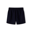 Close-up detail of cream pique polo shirt showing Minoti label, zip neck opening, navy collar and subtle embroidered logo on chest