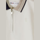 Close-up detail of cream pique polo shirt showing Minoti label, zip neck opening, navy collar and subtle embroidered logo on chest