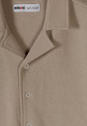 Detail of a boys' polo shirt in muted sand with a classic collar and button placket.