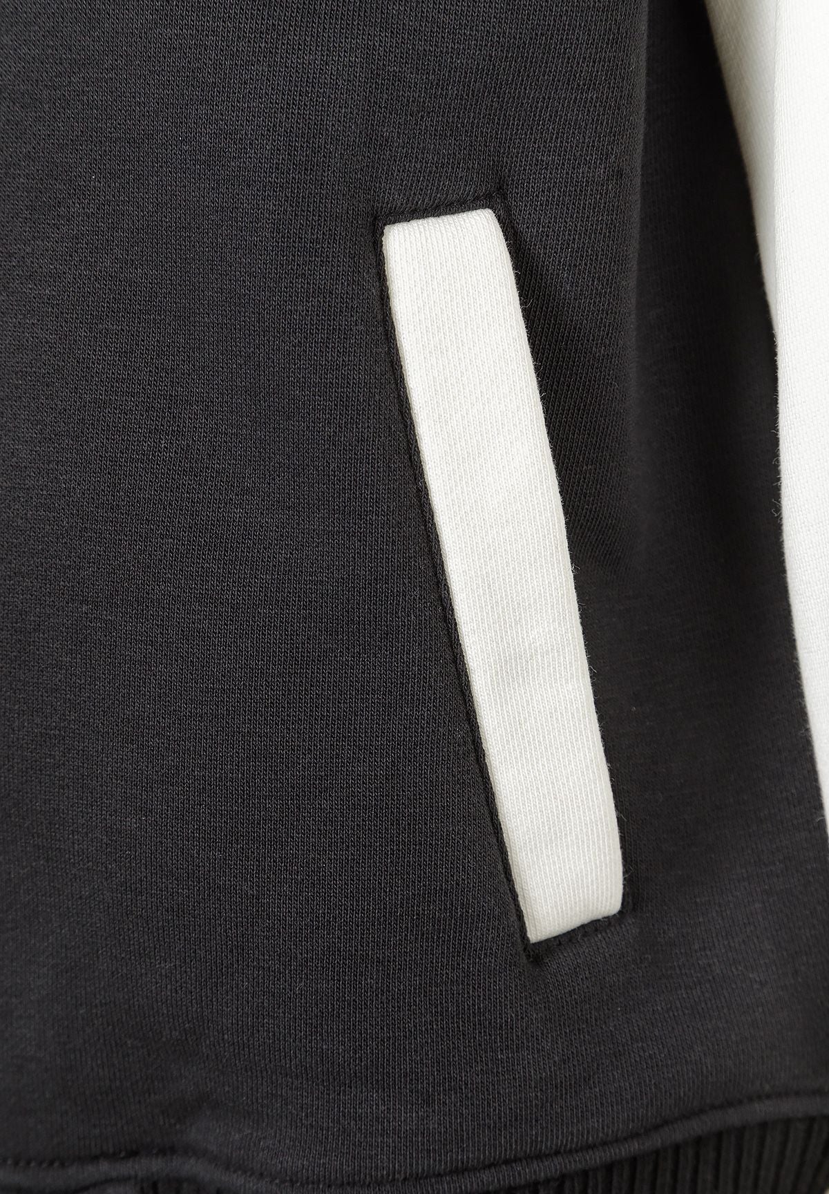 Detail of black baseball jacket with white pocket trim.