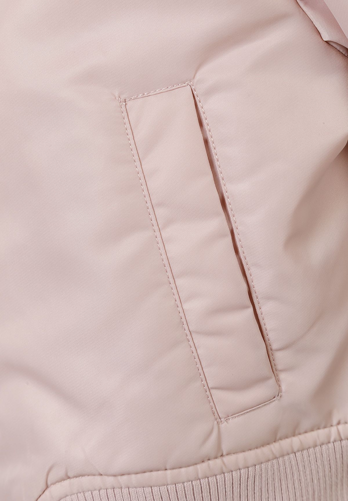 Close-up of the pocket on the light pink bomber jacket.