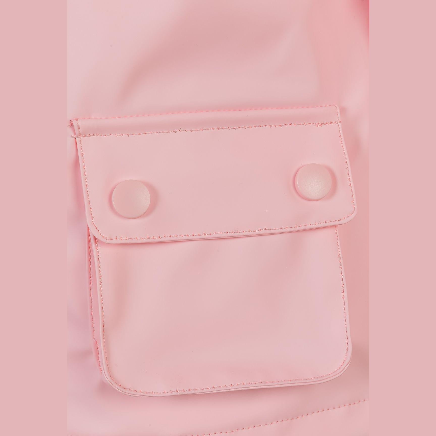 Close-up detail of pink rain jacket chest pocket with button flap closure, showing textured waterproof fabric and neat stitching against soft pink background