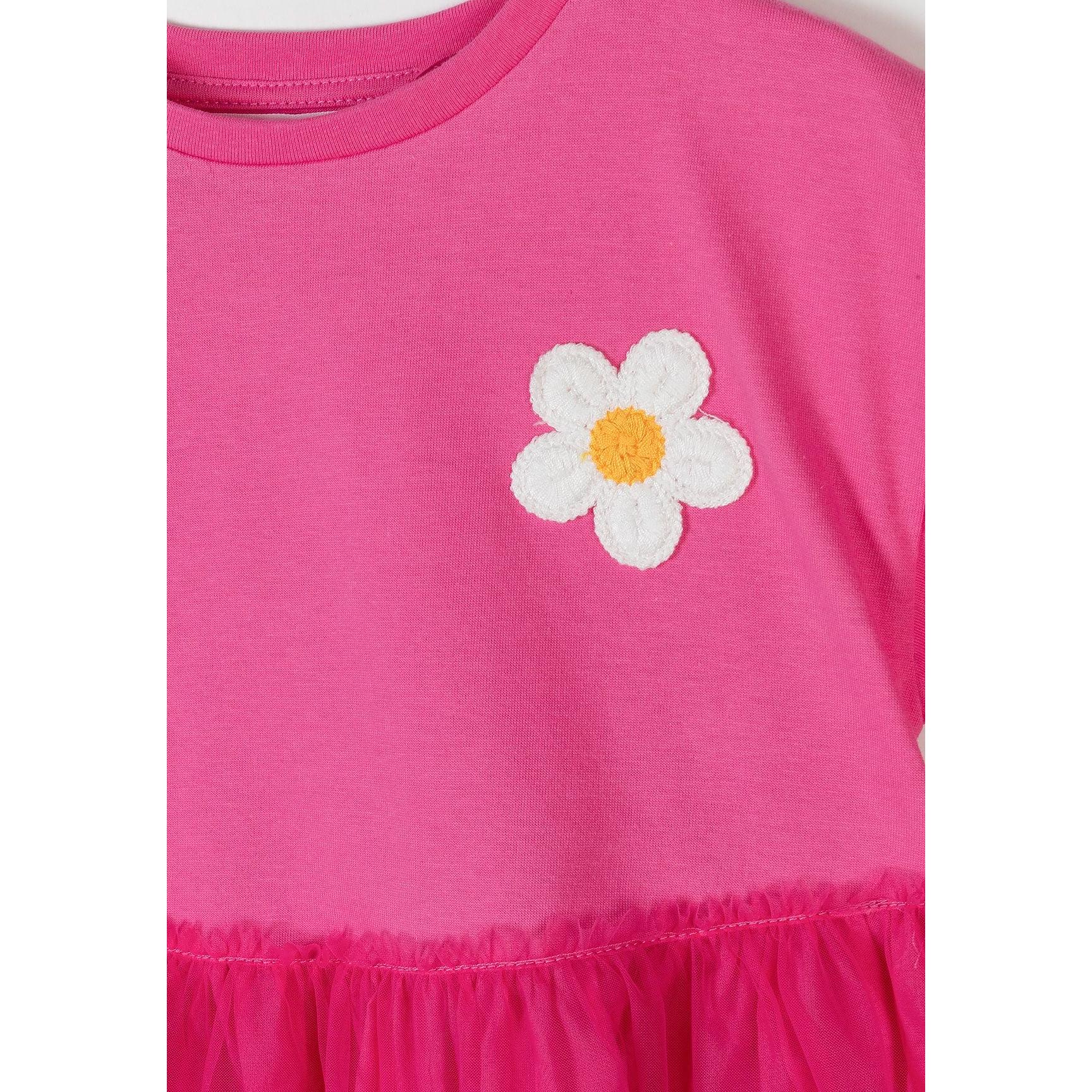 Close-up detail of white crochet flower with yellow centre on pink cotton jersey fabric showing texture and craftsmanship