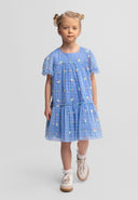 Young girl wearing blue tulle dress with floral embroidery and tiered skirt, walking against white background